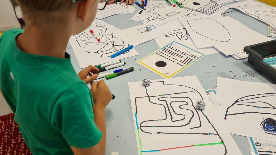 Letní příměstský tábor v Brně: Děti kreslí černými a barevnými fixami čáry, nebo trasy, po kterých jezdí malý robot